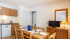 Eine kompakte Küche mit Holzausstattung, einem Esstisch für zwei Personen, einem Fernseher auf einem Holzständer und einer kleinen Kommode mit Spiegel.