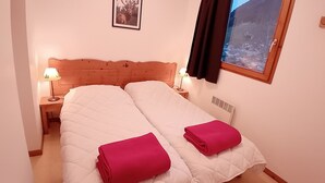 Ein Doppelbett mit weißer und rosa Bettwäsche, zwei Nachttische mit Lampen, ein gerahmtes Bild an der Wand und ein Fenster mit Bergblick.