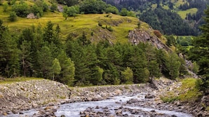Ein Fluss fließt durch eine gebirgige Landschaft mit dichten Wäldern und felsigem Gelände.