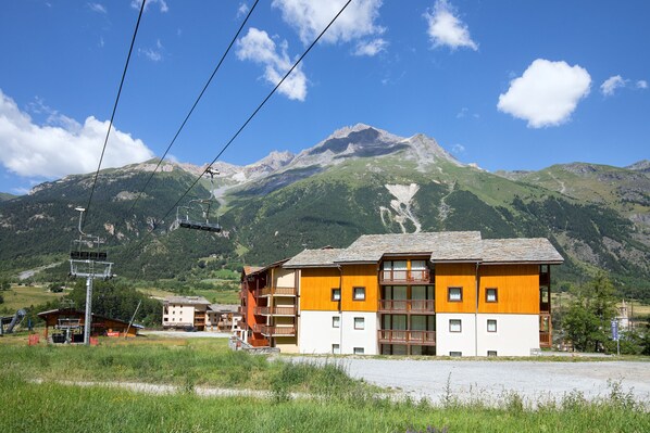A multi-story building with balconies, set against a mountainous backdrop. - Balcons B 015 - PARC NAT. VANOISE appart. 6 pers. (Val Cenis)