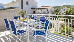 Terraço com mesa posta para o café da manhã, área de estar ao ar livre e vista para um edifício branco e vegetação.