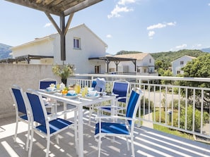Eine Terrasse mit Frühstückstisch, Gartenmöbeln und Blick auf ein weißes Gebäude und Grünflächen.