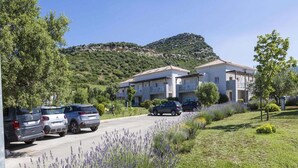 Um bairro residencial com edifícios de dois andares, um estacionamento cheio de carros e uma encosta ao fundo.