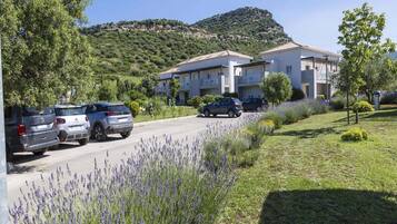 Zona residencial con edificios de dos pisos, un estacionamiento con coches y una colina al fondo.
