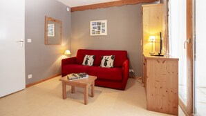 Een woonkamer met een rode bank, een houten tafel, een lamp en een kast.