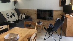 A cozy living room with a wooden dining table, chairs, a sofa with a cowhide cover, a fireplace, and a television.