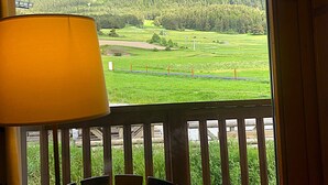 A balcony with a view of a mountainous landscape, a table with chairs, and a lamp.
