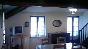 A dining area with a table and chairs, a television on a stand, and a staircase leading upstairs. - Cottage in the countryside, in the Tarn, between Aveyron and Hérault (Berlats)
