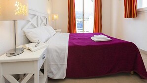Ein Hotelzimmer mit einem Bett, einem Nachttisch mit Lampe, einem Fenster mit Vorhängen und Blick nach draußen.