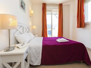 Ein Hotelzimmer mit einem Bett, einem Nachttisch mit Lampe, einem Fenster mit Vorhängen und Blick nach draußen.