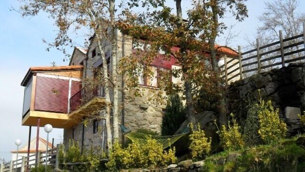 Un edificio de piedra con techo rojo, un balcón con toldo rojo y una valla de madera.