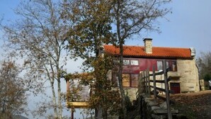 Una casa de piedra con techo de tejas rojas, una escalera de madera y vistas de los árboles circundantes.