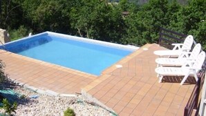Una piscina con solárium de baldosas y sillas reclinables blancas.
