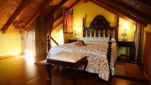 Un dormitorio con techo de madera, una cama con colcha estampada, una mesita de noche y una lámpara.
