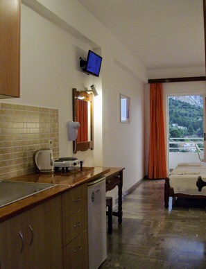 Habitación de hotel compacta con kitchenette, cama, una mesita y vista a un paisaje montañoso.