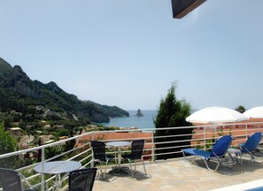 Una terraza con asientos al aire libre, vistas al mar y un paisaje montañoso.