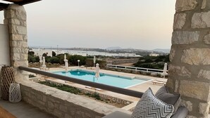 Un balcon en pierre avec une piscine, un canapé agrémenté de coussins à motifs et une vue sur le paysage.