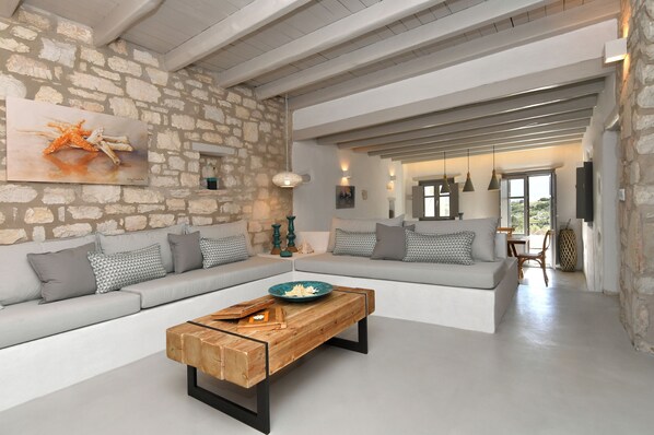 Amplia sala de estar con pared de piedra, una mesa de centro de madera y un sofá grande con cojines estampados.