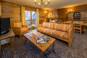 A cozy log cabin-style room with a sofa, a coffee table with magazines, a TV, and a dining area with a table and chairs.