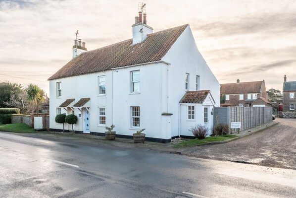 A white two-story house with a tiled roof, a front porch, and a small garden. - Samphire Cottage (BS), Brancaster Staithe, Norfolk (King's Lynn)