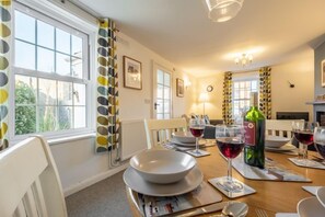 A dining area with a table set for four, a bottle of wine, and a clock on the wall.