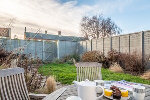 A wooden deck with a table set for breakfast, including a teapot, cups, and pastries. - Samphire Cottage (BS), Brancaster Staithe, Norfolk (King's Lynn)