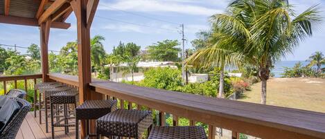 A wooden deck with wicker furniture, overlooking a beach and palm trees.