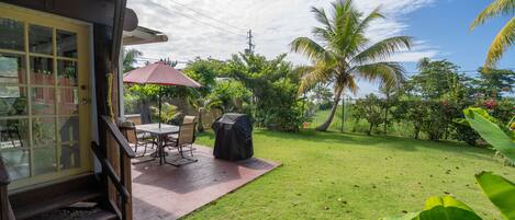 A patio with a table and chairs, a covered grill, and a red umbrella.