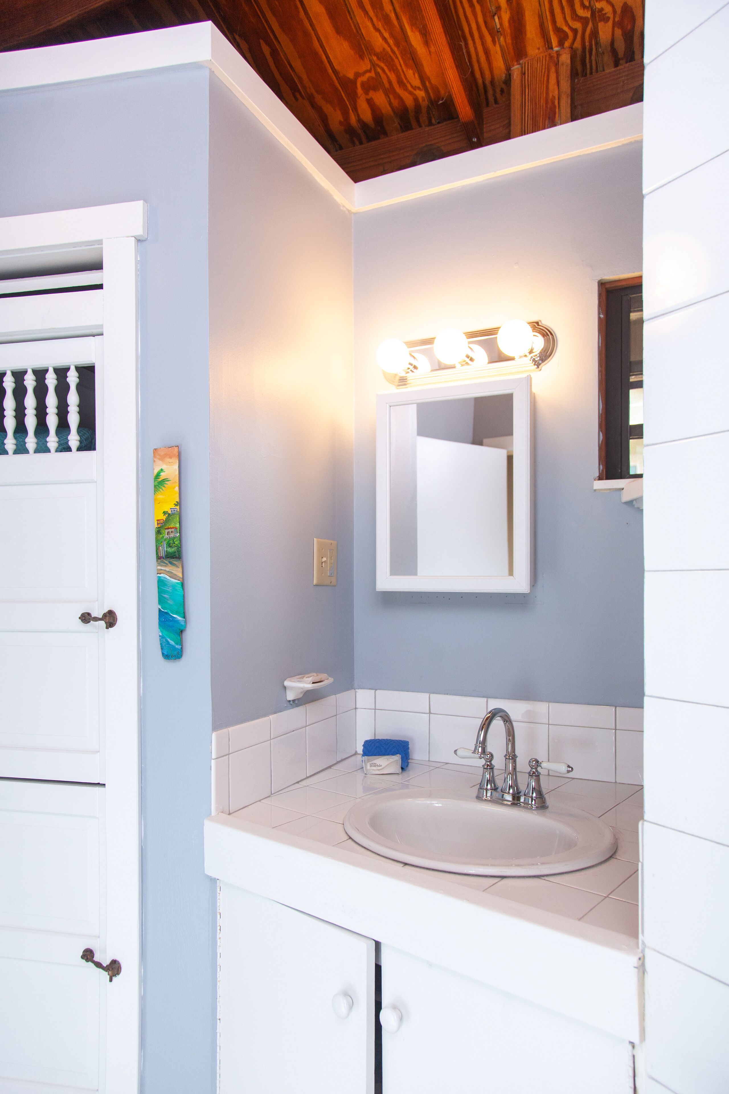 A bathroom with a white sink, a mirror, and a wooden ceiling.