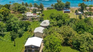 An aerial view of a coastal property with a large house, smaller buildings, and lush greenery.
