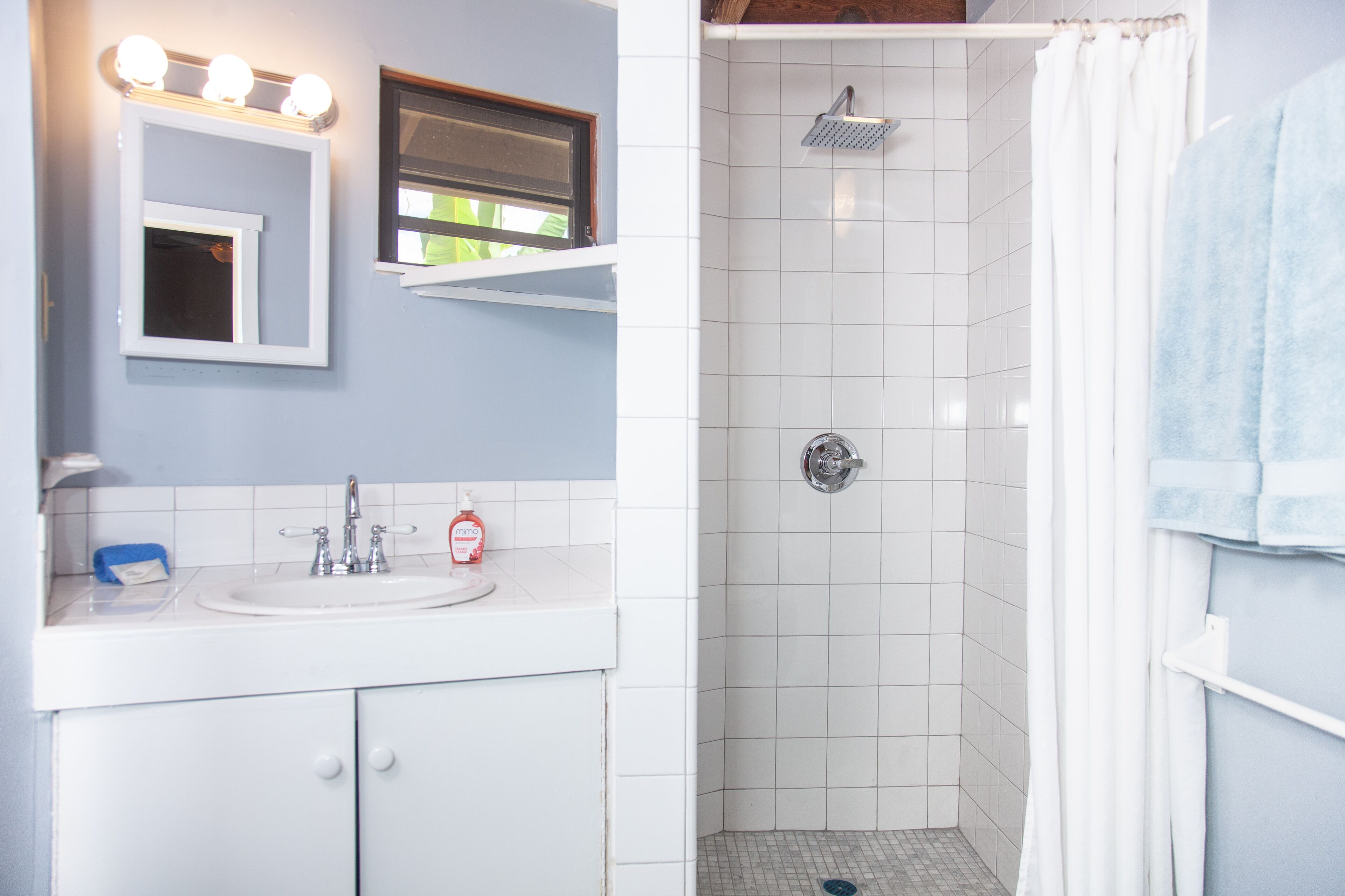 A bathroom with a white sink, mirror, and shower.