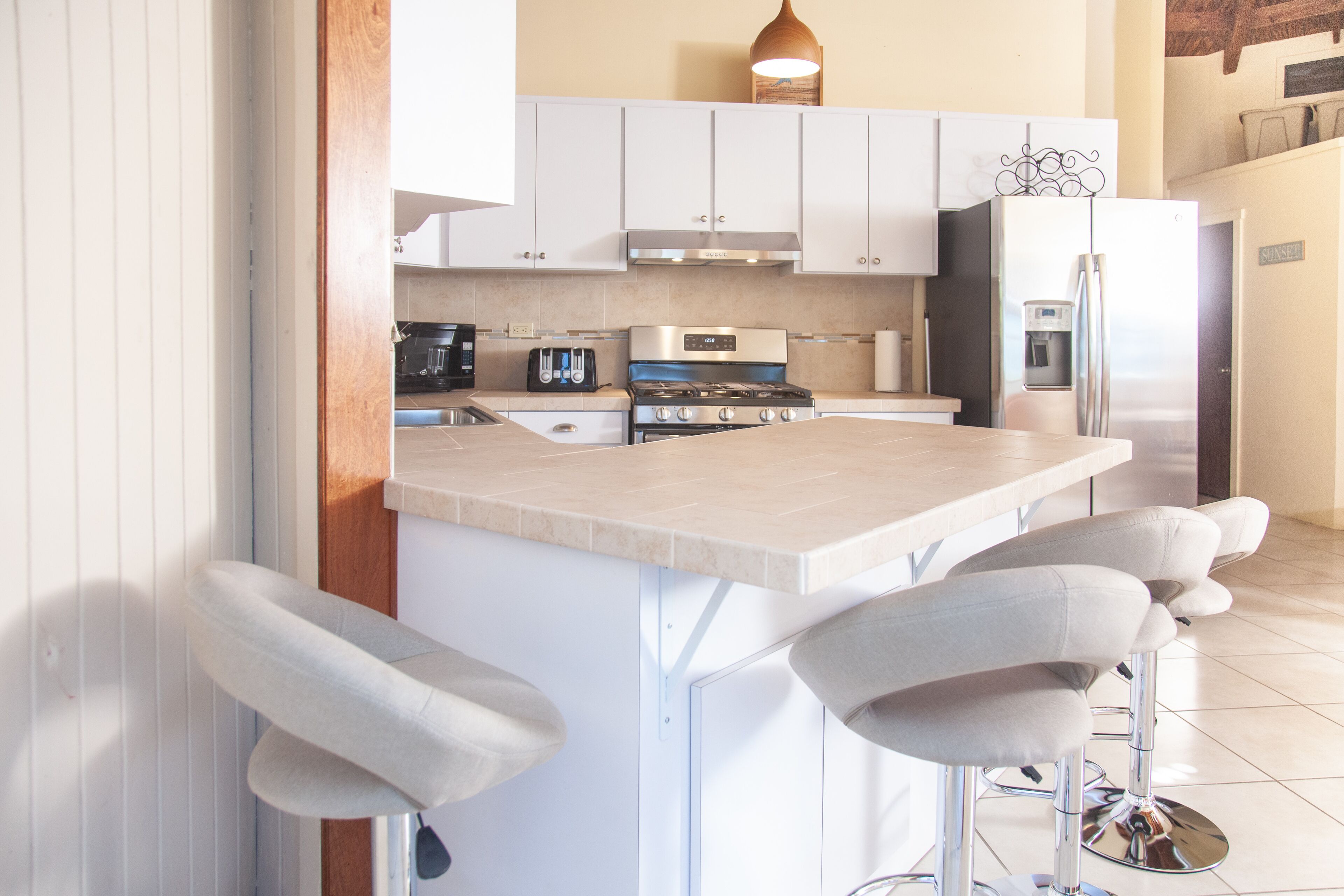 Cocina moderna con armarios blancos, refrigerador de acero inoxidable, horno empotrado y una zona con taburetes de bar.
