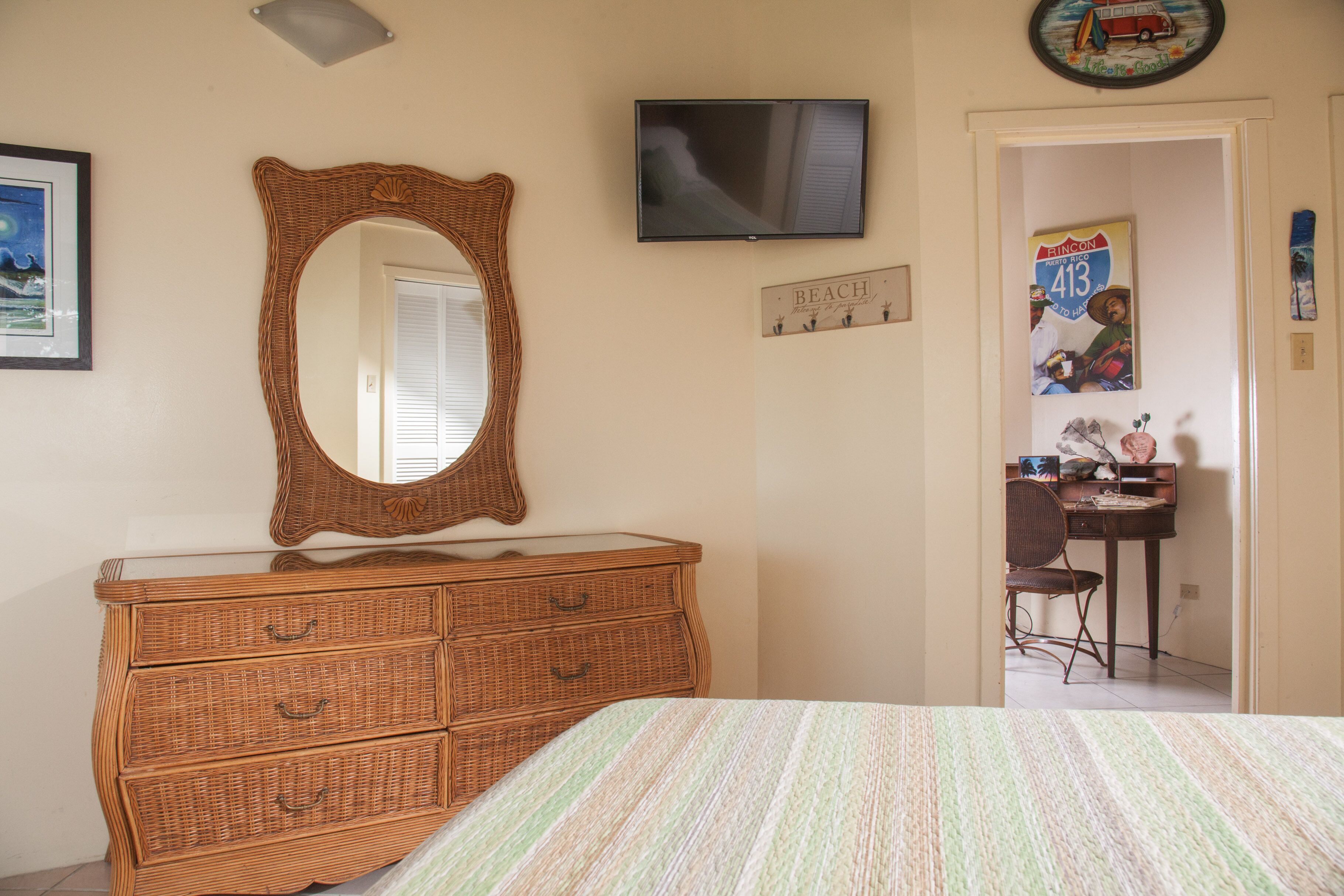 A bedroom with a bed, a dresser, a television, and a door leading to a bathroom.