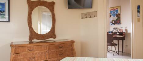 A bedroom with a bed, a dresser, a television, and a door leading to a bathroom.