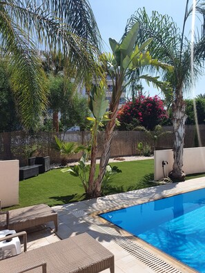 A swimming pool with a surrounding garden, outdoor furniture, and a fence.