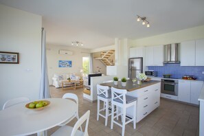 A modern kitchen with white cabinets, a central island, and a dining area with white chairs.