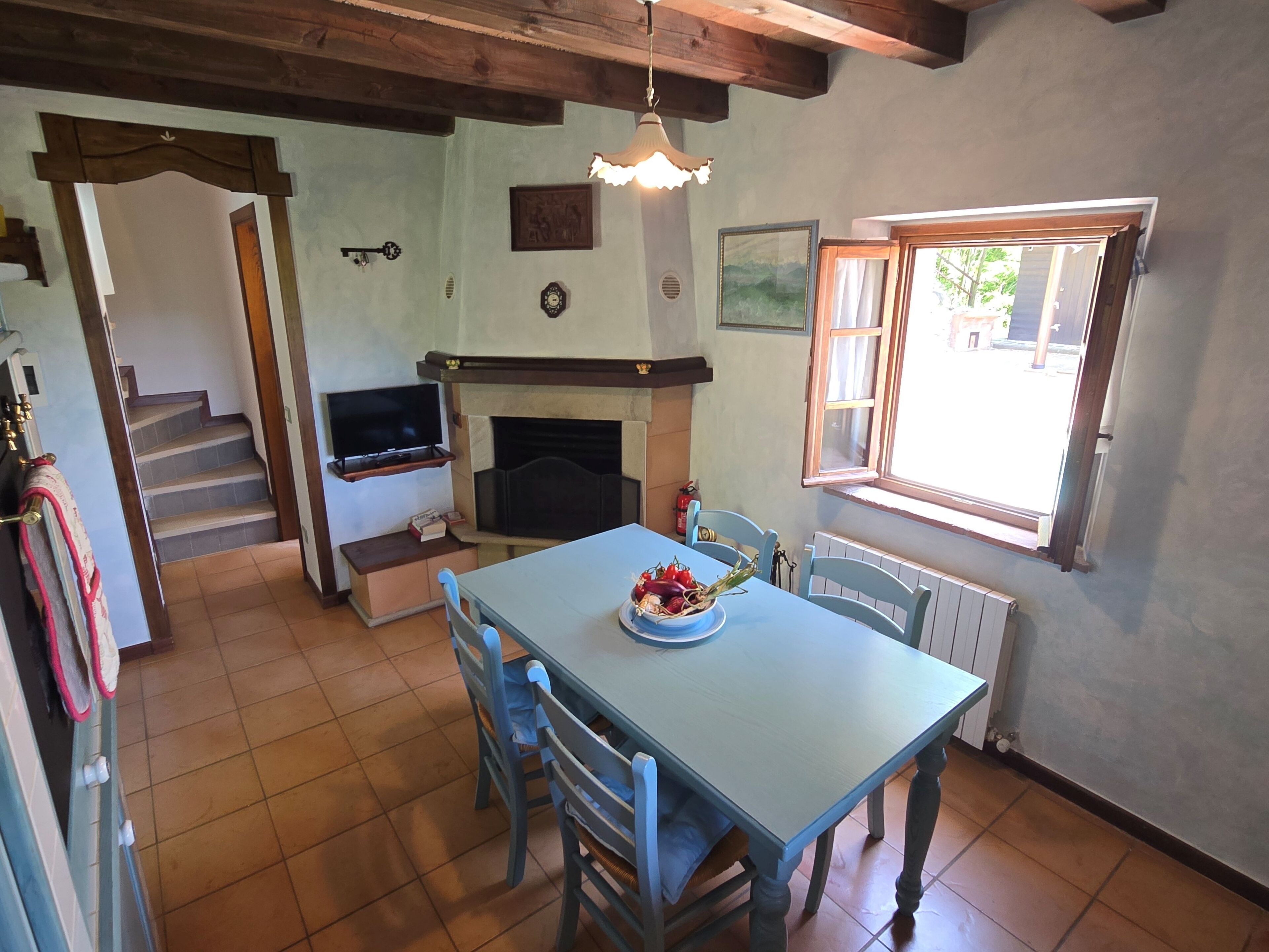 A dining area with a table and chairs, a fireplace, a television, and a window with a view of the outside.