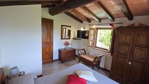 Un dormitorio con cama, armario de madera, cómoda, silla, espejo, ventana y televisor.