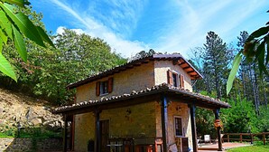 Una casa de piedra con techo de tejas, un patio con mobiliario exterior y una pared de piedra al fondo.
