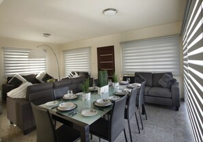A dining area with a table set for four, surrounded by sofas, a floor lamp, and a potted plant.