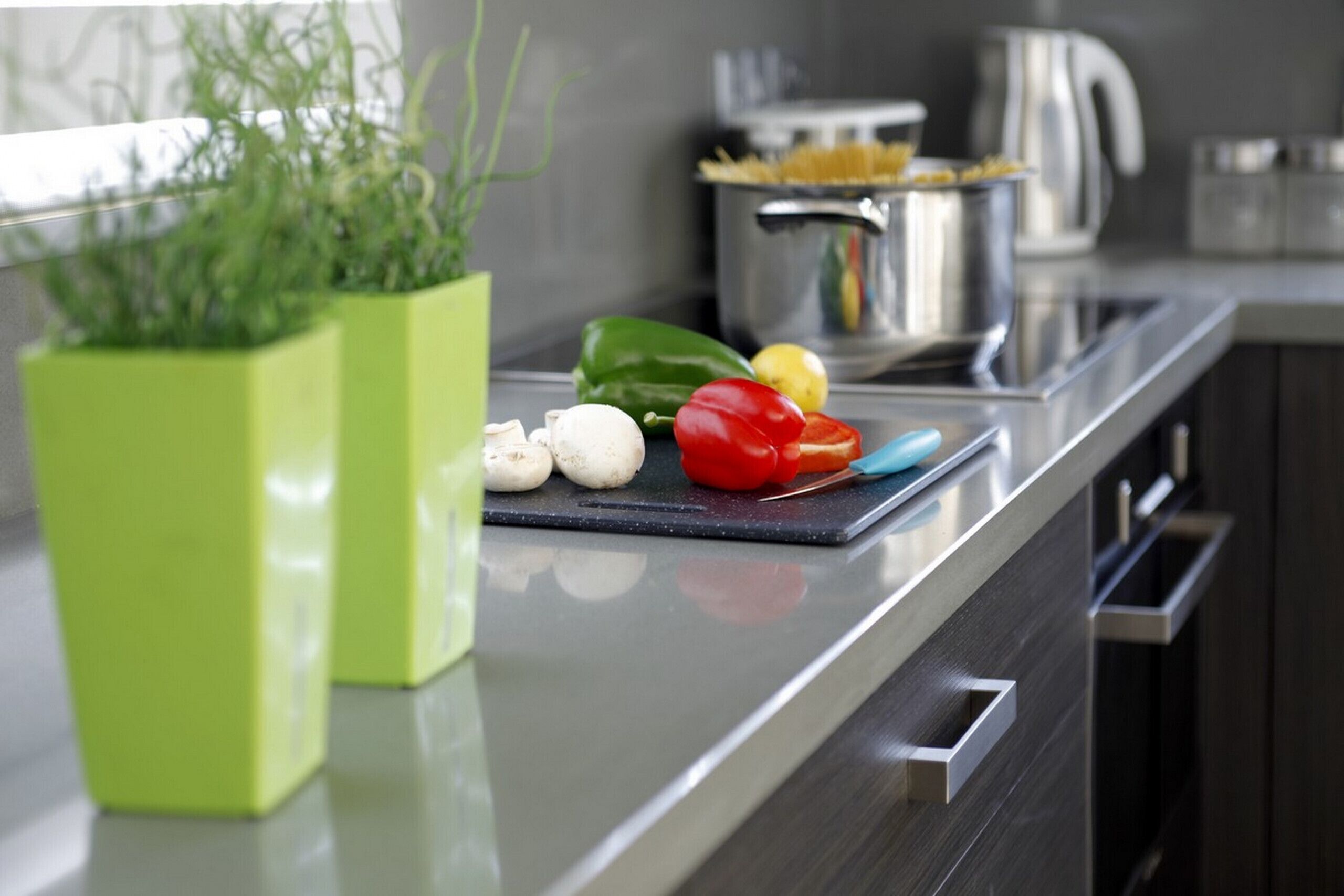Un plan de travail de cuisine avec une planche à découper, des légumes, une casserole et une bouilloire.