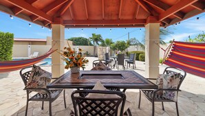 An outdoor patio with a table and chairs, a hammock, and a pool in the background. - PALM BEACH LUXURY VACATION  VILLA !!!!! (Palm beach)