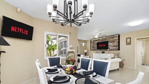 A dining area with a table set for four, a chandelier, and a television displaying the Netflix logo. - PALM BEACH LUXURY VACATION  VILLA !!!!! (Palm beach)