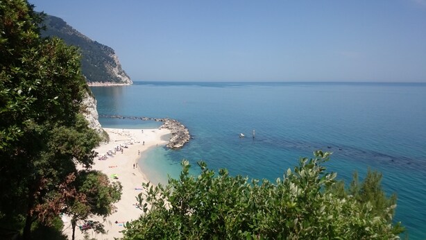 A beach with clear blue water, rocky shoreline, and lush greenery. - Natural stone country house (Arcevia)