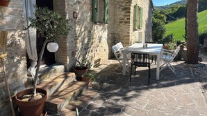 A stone building with a patio, outdoor seating, and a view of green hills. - Natural stone country house (Arcevia)