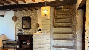 A rustic interior with a stone wall, a wooden staircase, a mirror, and a small wooden stool. - Natural stone country house (Arcevia)