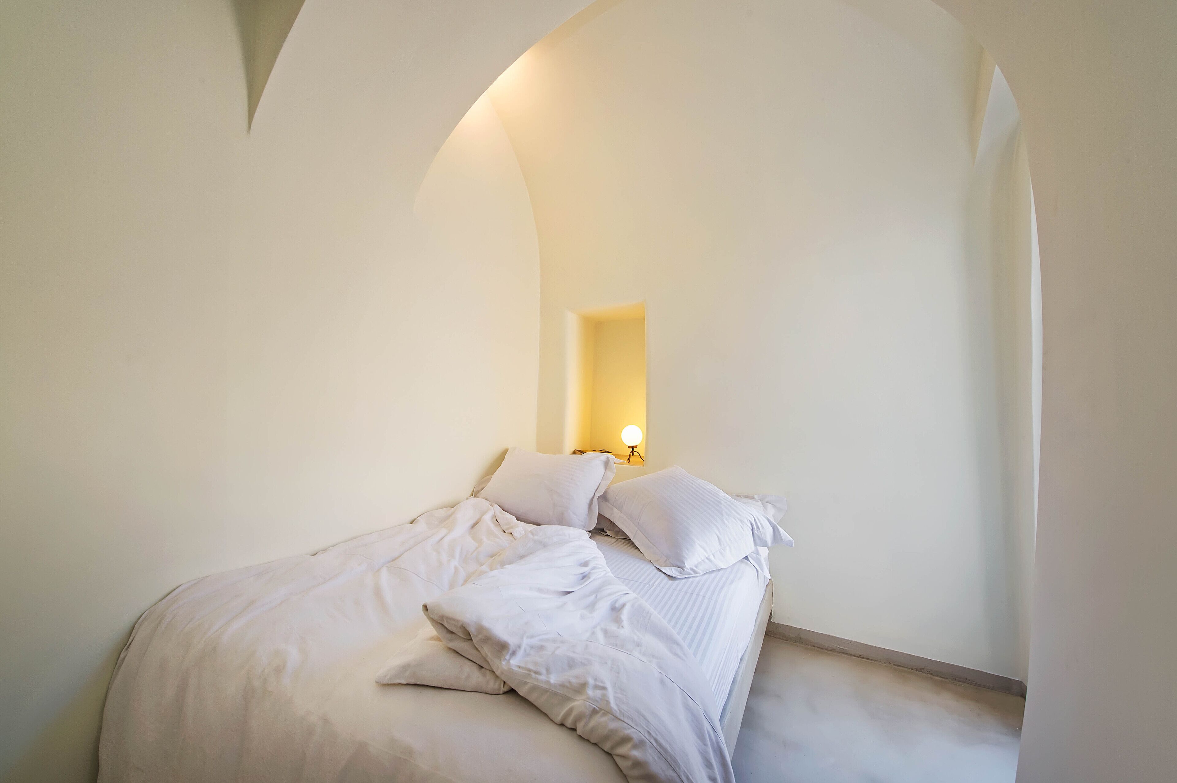 A bedroom with a bed, pillows, and a wall-mounted light fixture.
