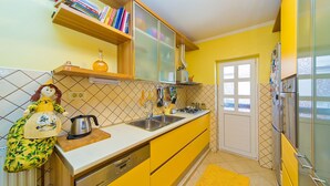 A kitchen with yellow cabinets, a sink, a stove, and a refrigerator. There is a window with a view of the outside. - Spacious 5 bedroom Stone Villa with Private Pool and Sea view  (Mlini)