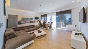 A modern living room with a large sectional sofa, a dining area with a table and chairs, and a kitchen in the background. - Spacious 5 bedroom Stone Villa with Private Pool and Sea view  (Mlini)