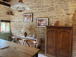 A rustic dining area with a wooden table and chairs, a lamp, and a cabinet against a stone wall. - Perigordian house,quiet,and ECOLOGICAL PRIVATE SWIMMING POOL natural water, WIFI (Tourtoirac)